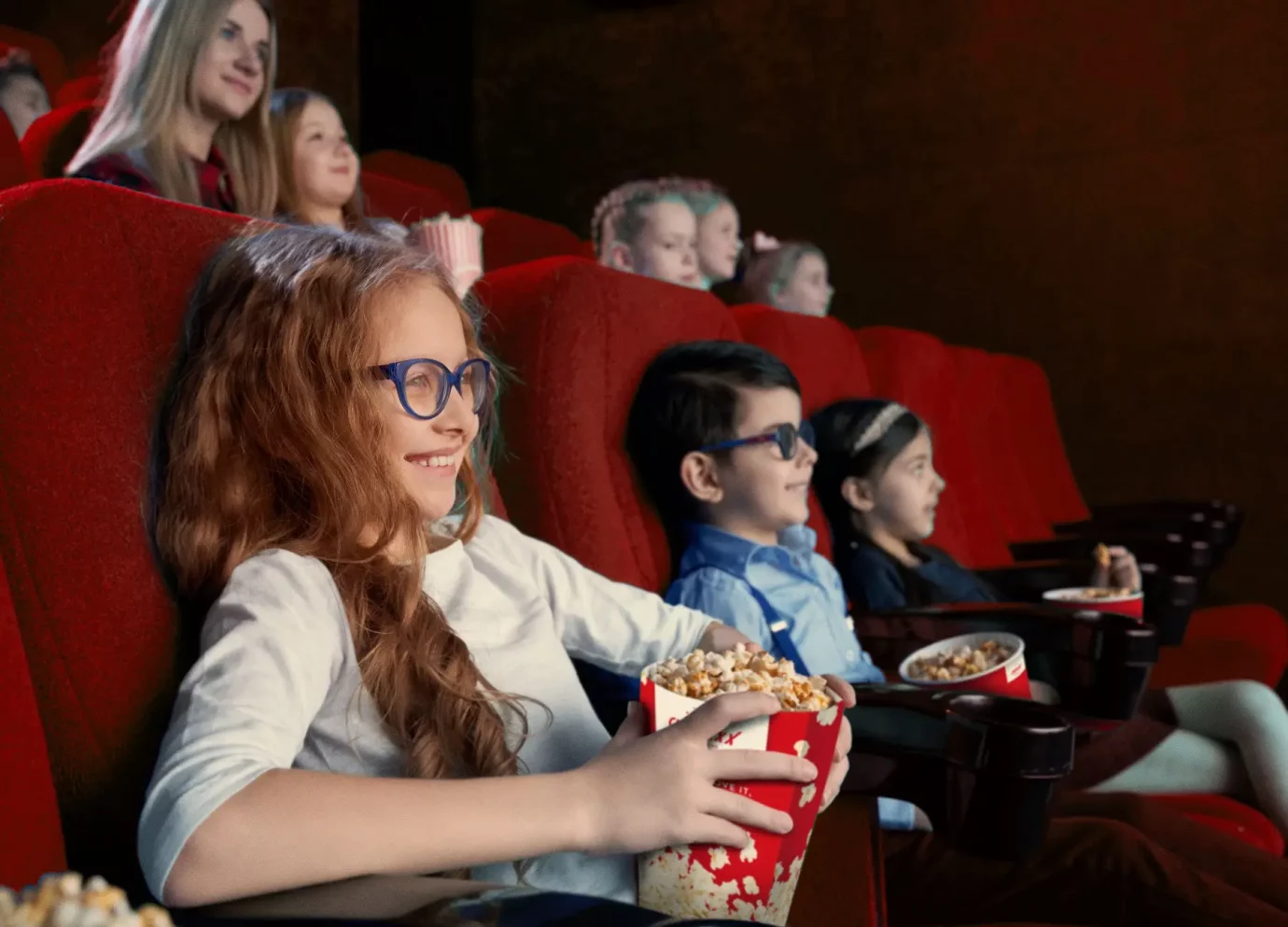 Kinder die im Kino sind und sich einen Film ansehen während sie Popcorn essen.