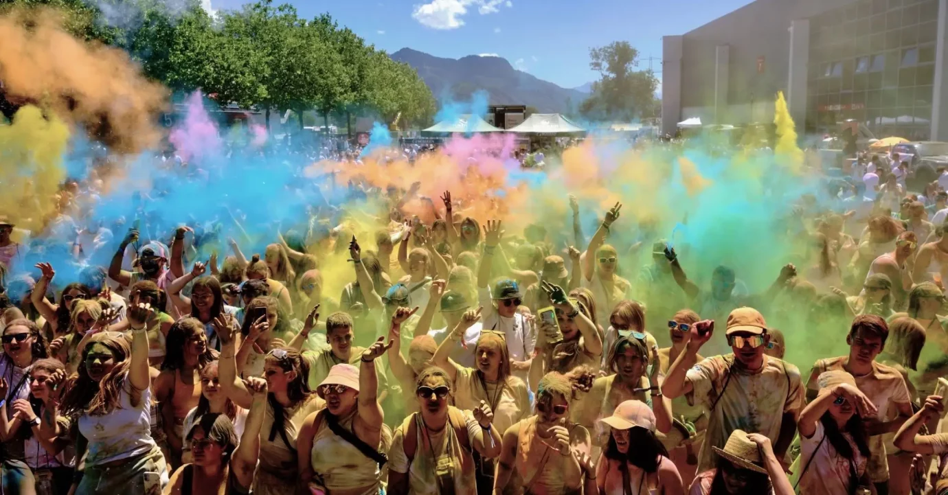 Besucher und Besucherinnen von dem Holi Flash Festival in Dornbirn wie sie die Pulverfarben in die Luft werfen